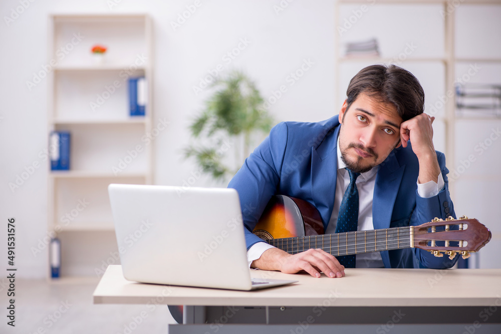 Young male employee playing guitar at workplace Young male employee playing guitar at workplace