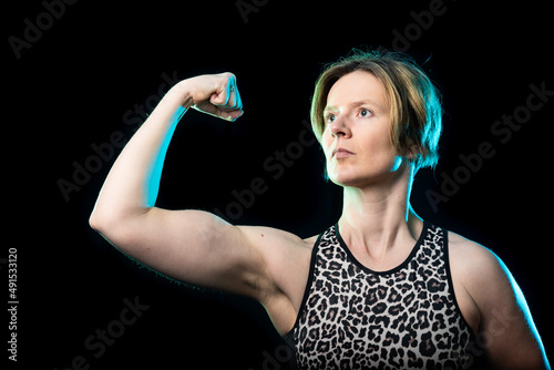 Low key studio portrait of a 35 year old white woman showing her biceps