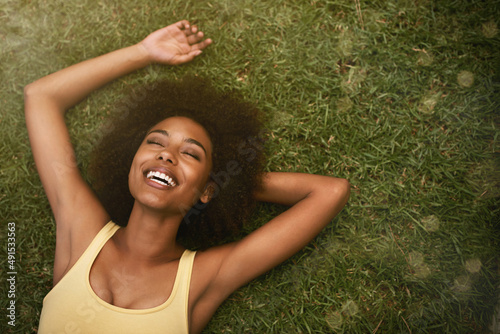 This is the life. Shot of a young woman laughing while relaxing on the grass. photo