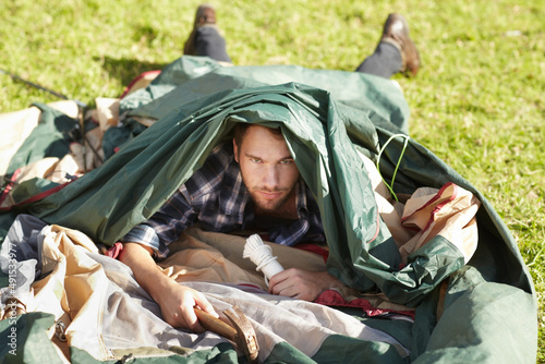 Hes clearly an amateur camper. Frustrated young man struggling to erect a tent outdoors. photo
