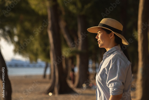 Young asian woman with straw hat standing alone on beach looking at sunset seashore. Chilling in holiday weekend summertime. Traveler Female walking around the beach with the sunlight © Chanakon