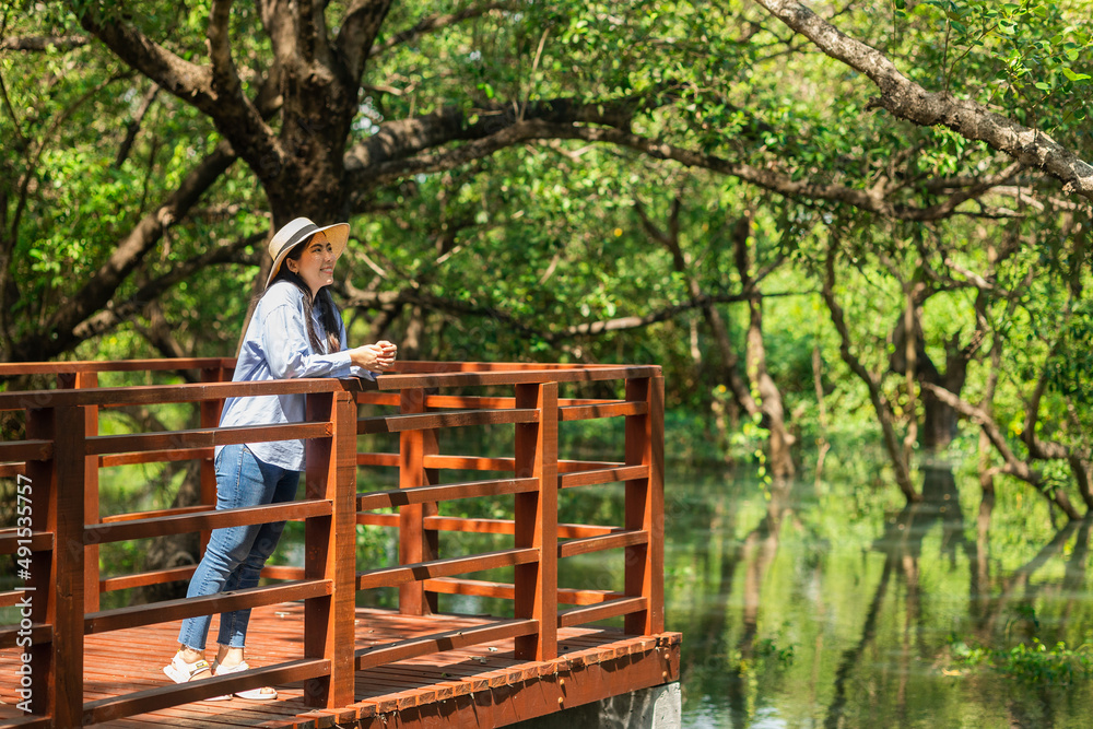Young asian woman travel in the middle of nature with sunlight. Traveller blogger in mangrove forest. Rest on vacation holiday weekend. Beautiful female with hat and blue shirt walking in forest Young asian woman travel in the middle of nature with sunlight. Traveller blogger in mangrove forest. Rest on vacation holiday weekend. Beautiful female with hat and blue shirt walking in forest