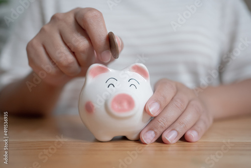 Woman hands holding and putting Thai currency coin into piggy bank. Saving concept with piggy bank at home.