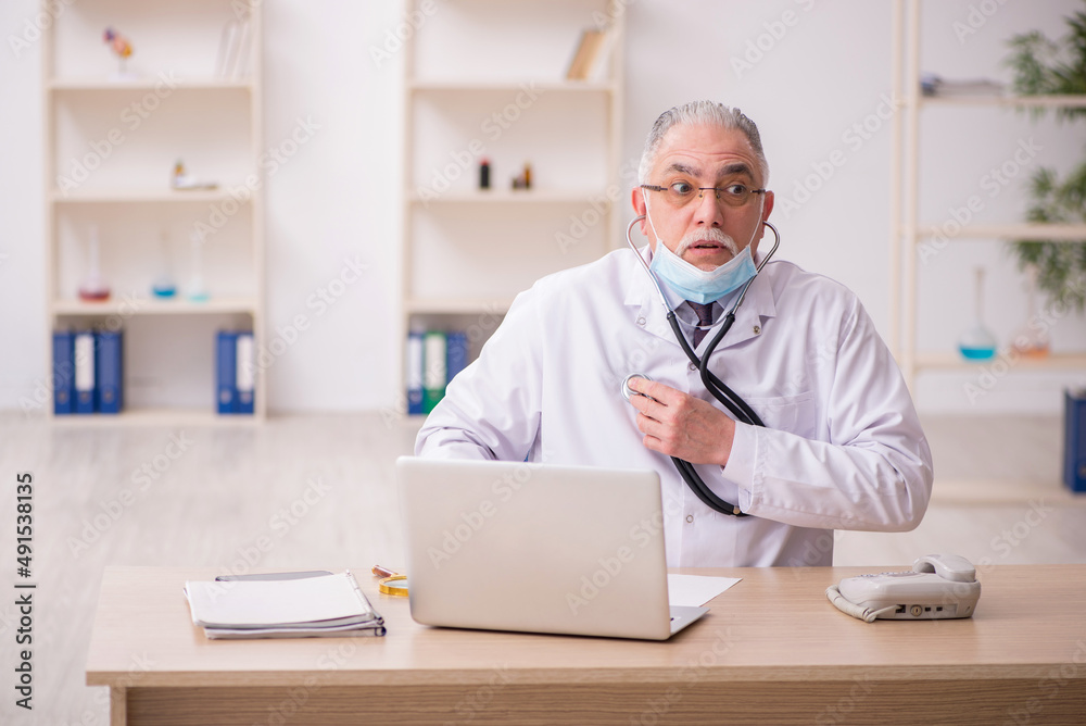 Old male doctor working in the clinic during pandemic Old male doctor working in the clinic during pandemic