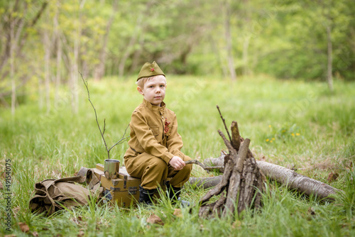 a small child in a beautiful military victory uniform, playing in nature and eating soldier porridge