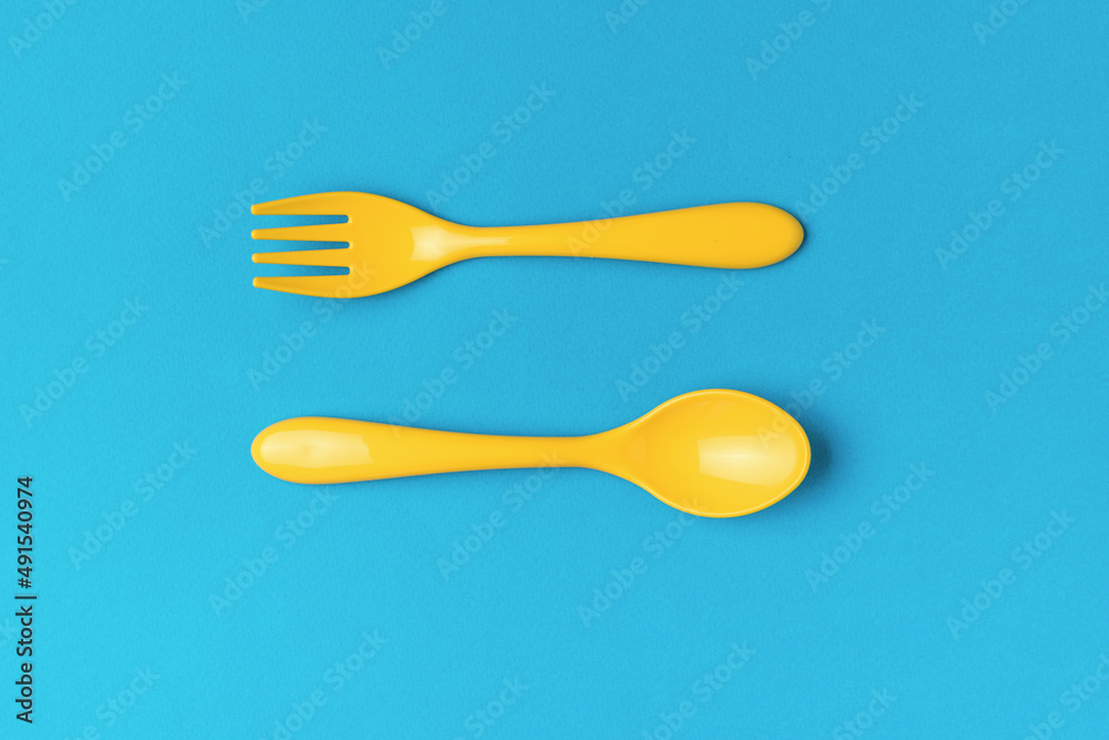 A set of yellow plastic spoon and fork on a blue background. Flat lay. A set of yellow plastic spoon and fork on a blue background. Flat lay.