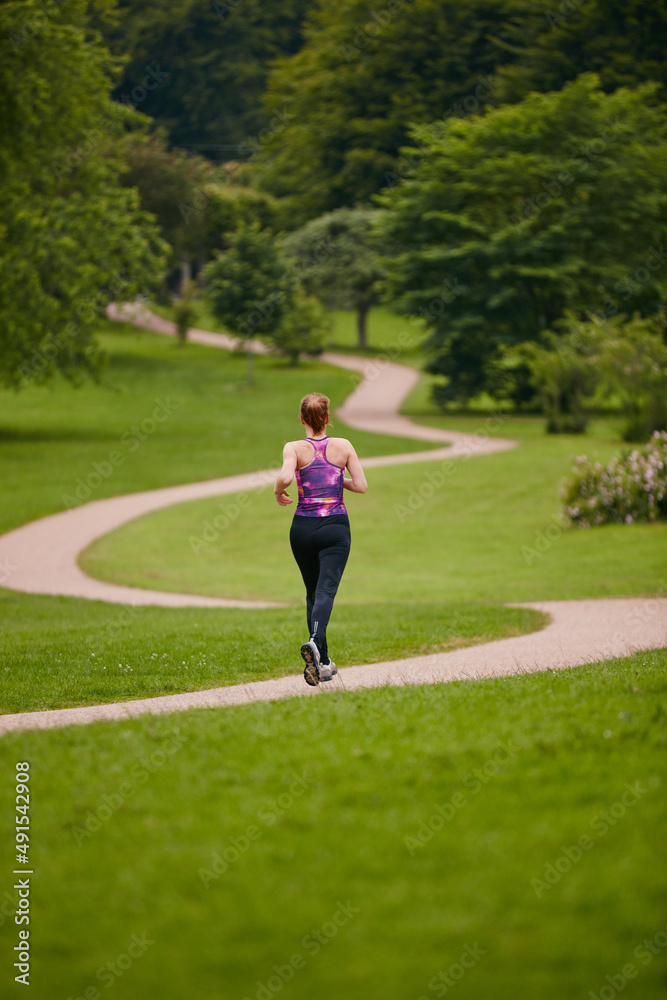 In it for the long run. Rearview shot of a woman jogging along a foothpath in a park.