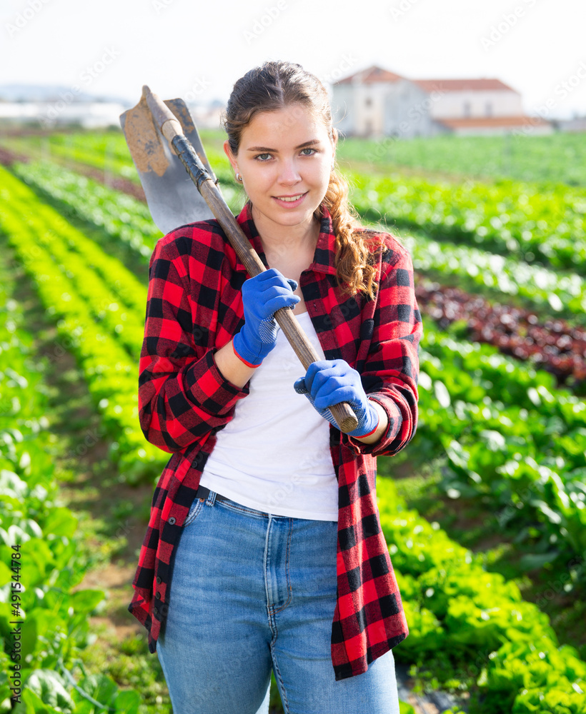 Attractive female farmer standing on farm field with hoe in her hands ...