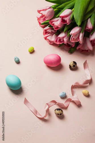 easter greeting card concept. bouquet of pink tulips with set of varios pastel colorful egss, pink ribbon on pink backround. Easter background. top view with copyspace