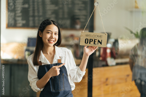 Asian Happy business woman is a waitress in an apron, the owner of the cafe stands at the door with a sign Open waiting for customers. Small business concept, cafes, and restaurants