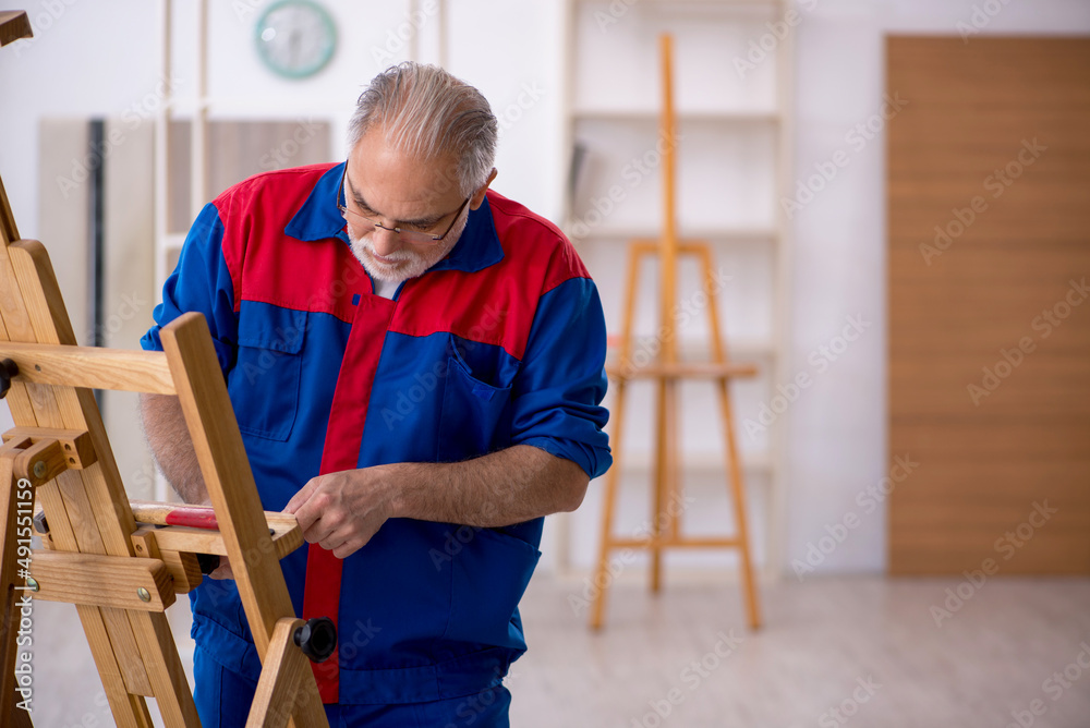 Old male carpenter repairing drawing easel Old male carpenter repairing drawing easel