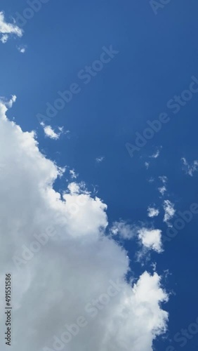 Timelapse of a fluffy cumulus cloud formation with sunlight, clear blue sky and shade, vertical video photo