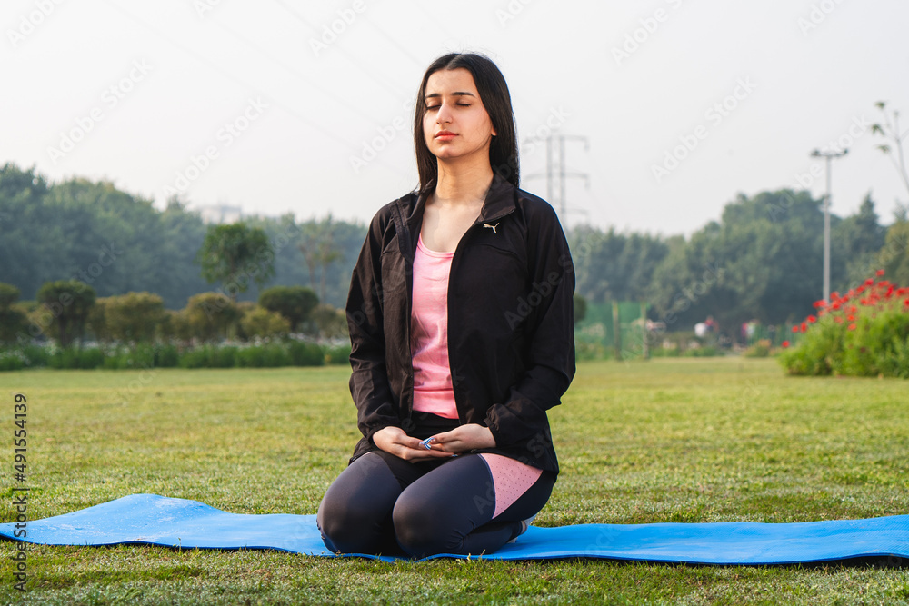 Young indian girl meditating in the park early in the morning. Girl working out in the morning. Healthy lifestyle concept. Young indian girl meditating in the park early in the morning. Girl working out in the morning. Healthy lifestyle concept.
