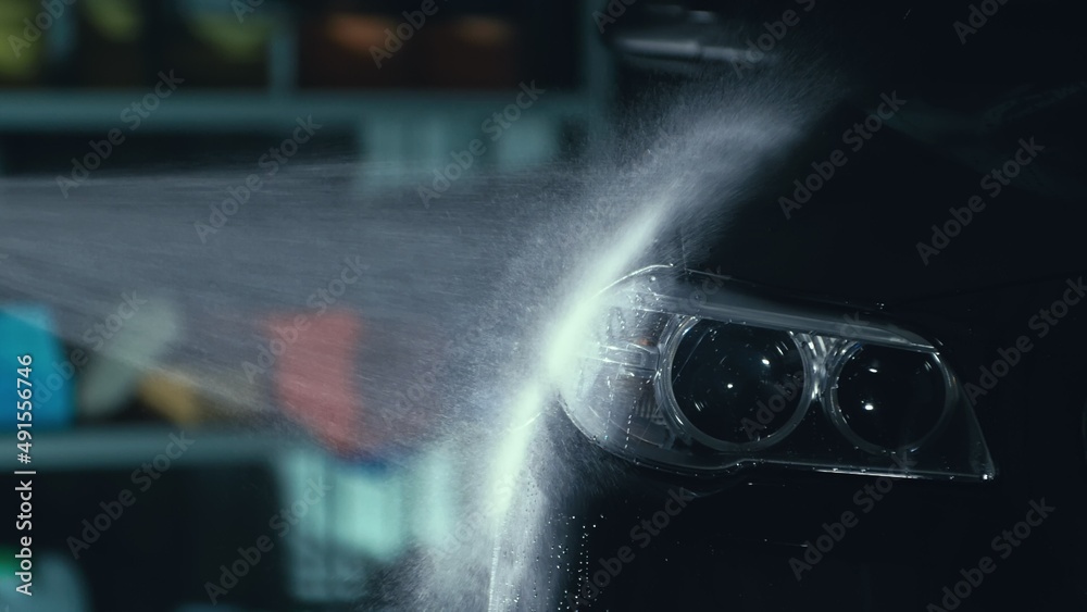 Car headlight wash. Washing modern vehicle body by high pressure jet