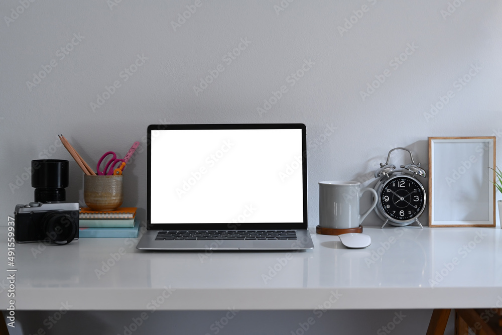 Front view computer laptop, stationery, alarm clock and picture frame on white table. Front view computer laptop, stationery, alarm clock and picture frame on white table.
