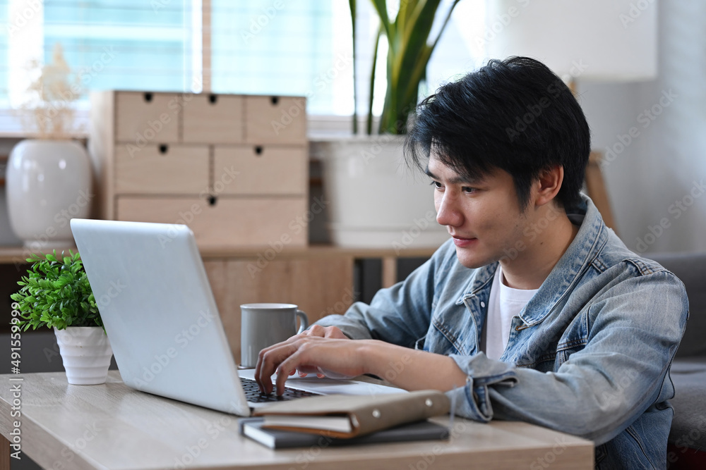 Fototapeta premium Asian male freelancer sitting on floor in living room and working online with laptop.