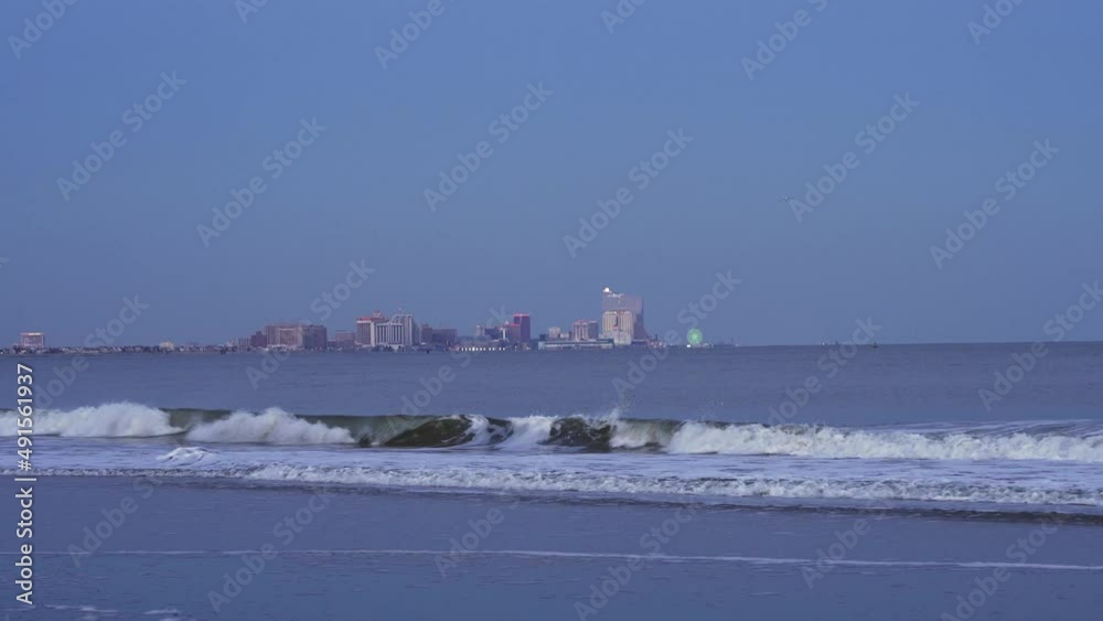 Ocean waves rolling and buildings in Atlantic City New Jersey in the distance, sunset blue hour Ocean waves rolling and buildings in Atlantic City New Jersey in the distance, sunset blue hour