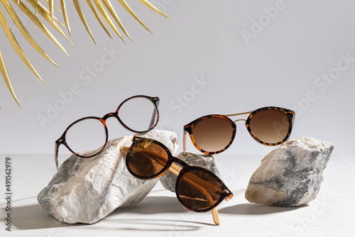 Sunglasses and glasses sale concept. Trendy sunglasses on gray background with golden palm leaves. Trendy Fashion summer accessories. Copy space. Summer sale. Optic store discount poster