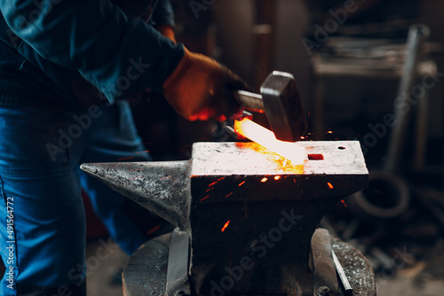 Blacksmith forges and makes metal detail with hammer and anvil at forge