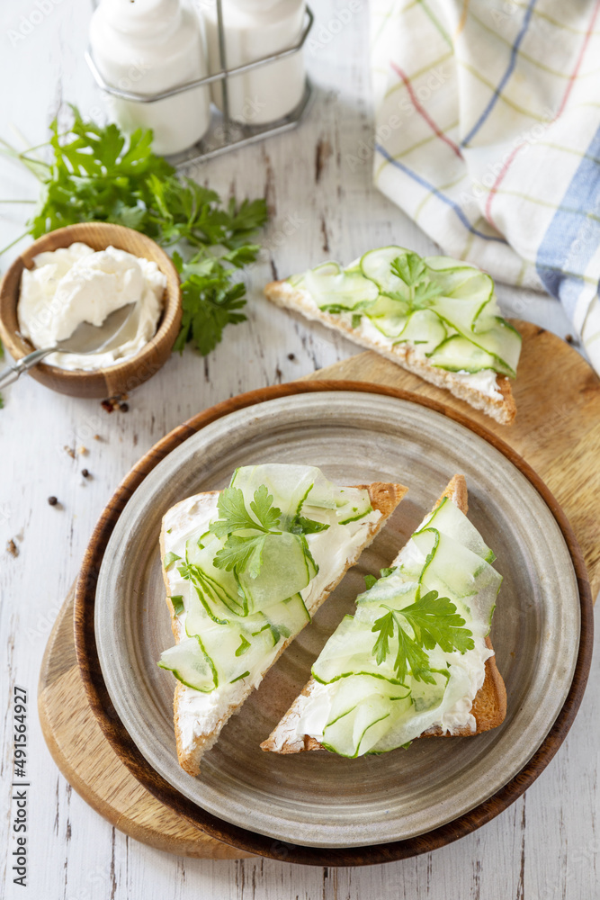 Healthy breakfast or holiday snacks. Toast with cucumbers, herbs and ricotta on a rustic wooden table.