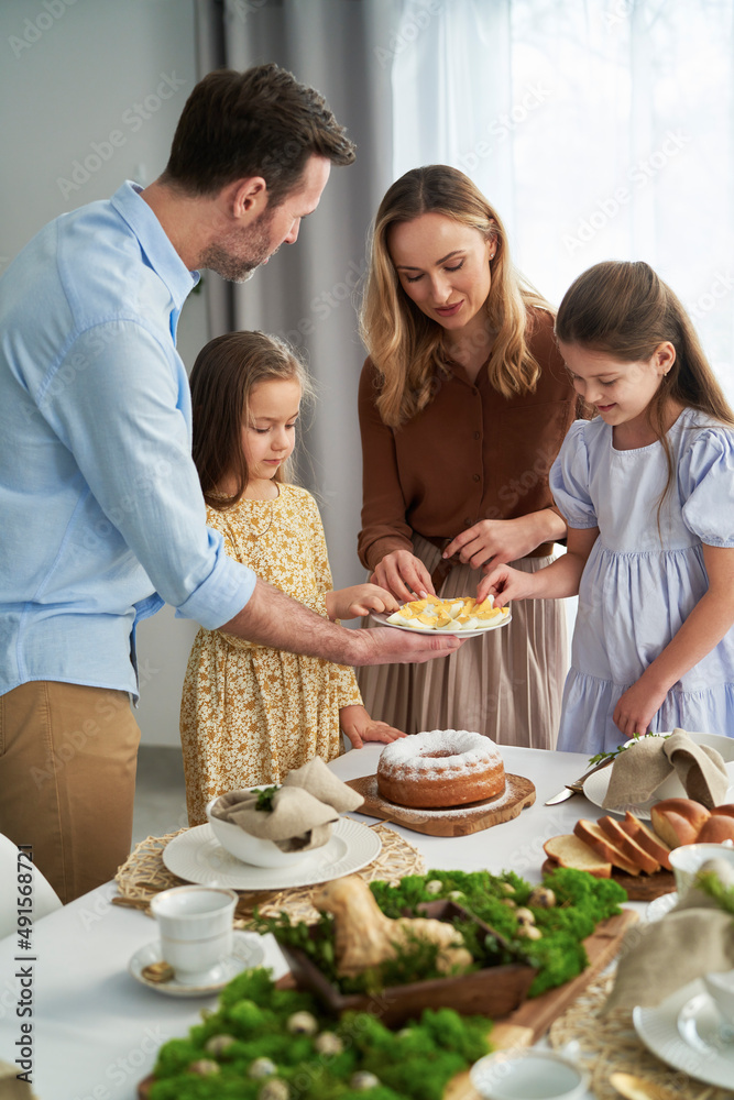 Vertical image of cheerful caucasian family of four sharing with egg during easter dinner