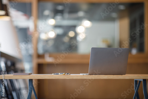 Laptop Computer, notebook, and eyeglasses sitting on a desk in a large open plan office space after working hours photo