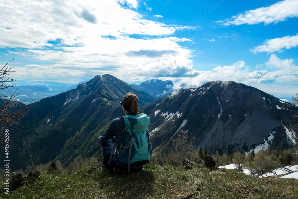 Female hiker having a break in spring on the summit of Frauenkogel in the Karawanks in Carinthia, Austria, Europe. Borders with Slovenia. Triglav National Park. Looking on Kahlkogel and Hahnkogel.