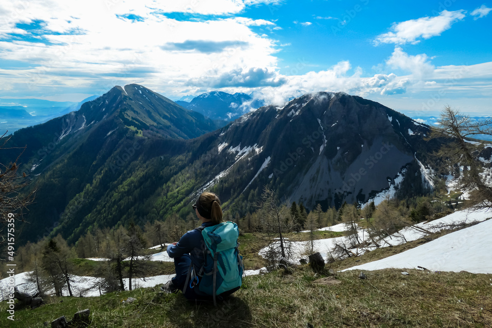 Female hiker having a break in spring on the summit of Frauenkogel in the Karawanks in Carinthia, Austria, Europe. Borders with Slovenia. Triglav National Park. Looking on Kahlkogel and Hahnkogel. Female hiker having a break in spring on the summit of Frauenkogel in the Karawanks in Carinthia, Austria, Europe. Borders with Slovenia. Triglav National Park. Looking on Kahlkogel and Hahnkogel.