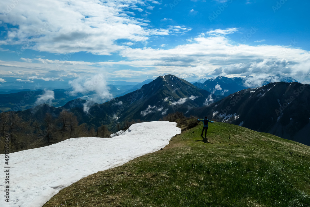 Active man hiking on Frauenkogel with scenic view on mountain peaks in the Karawanks, Carinthia, Austria. Border with Slovenia. Triglav National Park. Kahlkogel (Golica). Snow field melting in spring