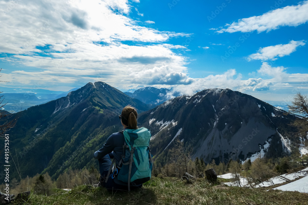 Naklejka premium Female hiker having a break in spring on the summit of Frauenkogel in the Karawanks in Carinthia, Austria, Europe. Borders with Slovenia. Triglav National Park. Looking on Kahlkogel and Hahnkogel.
