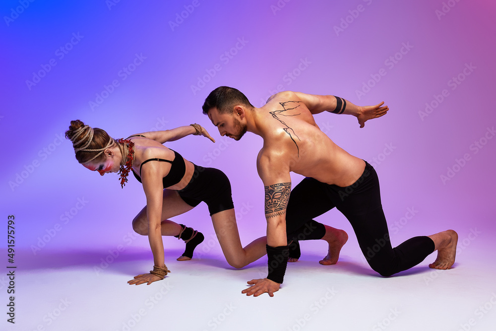 Beautiful young acrobats or gymnasts with colorful face painting on pink blue gradient background. Professional ballet couple dancing, Emotional duet performing choreographic art. Animal instinct