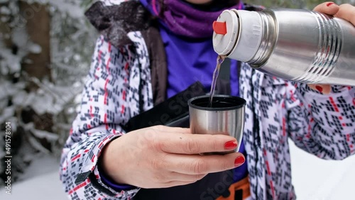 Woman pours water from a thermos In the winter Carpathians at hiking, Romania. Woman stopped while climbing Giumalau peak. Snow forest around photo