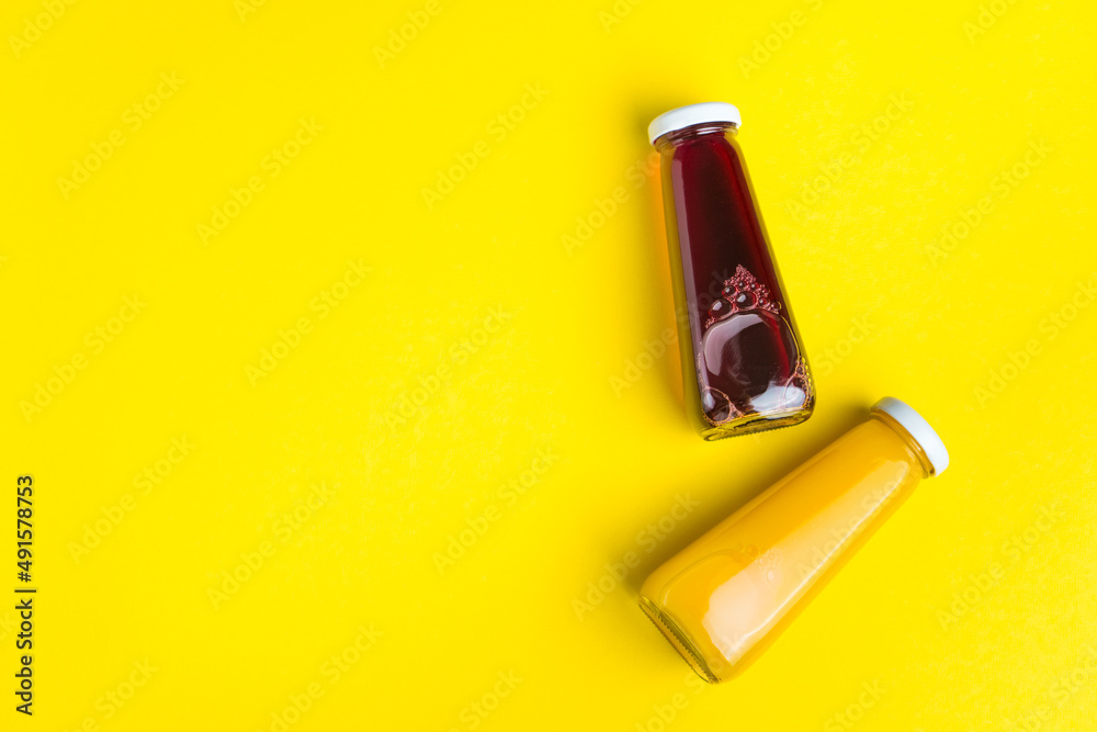 Bottles with yellow and red liquid halthy beverage on yellow background. Orange and cherry juice Bottles with yellow and red liquid halthy beverage on yellow background. Orange and cherry juice