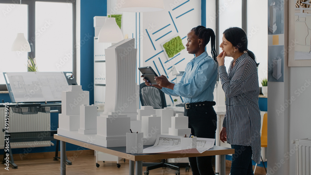 Architects analyzing building model with digital tablet to work on construction layout. Team of diverse women using device and technology to design real estate plan in architectural office. Architects analyzing building model with digital tablet to work on construction layout. Team of diverse women using device and technology to design real estate plan in architectural office.