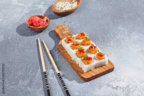 Maki roll with salmon and tobiko caviar on wooden board in contemporary composition. Sushi roll with chopsticks on concrete table. Maki sushi with salmon top in minimal style.