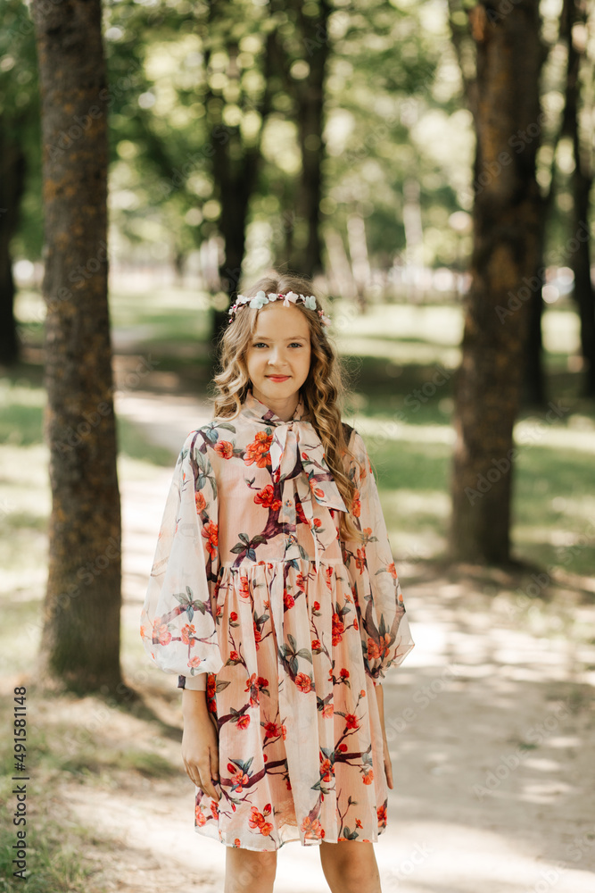 Smiling blonde teen girl posing in summer garden. Wearing flower wreath outdoors. Smiling blonde teen girl posing in summer garden. Wearing flower wreath outdoors.