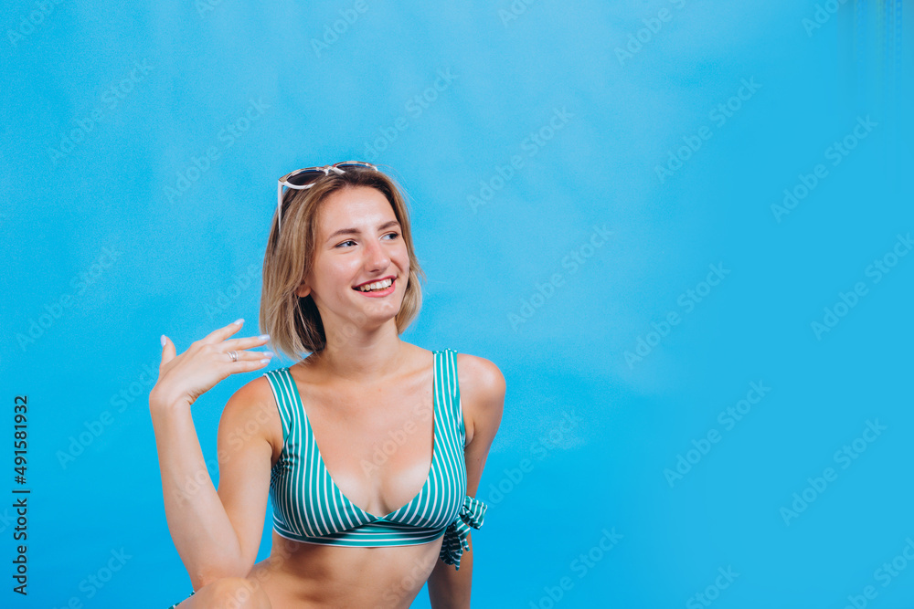 portrait of a beautiful girl in a bathing suit. girl is smiling and has sunglasses. photo on a blue background. beach summer vacation