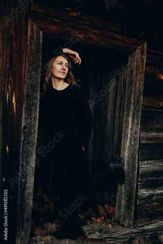 beautiful Ukrainian girl in black clothes near the old wooden house. The war in Ukraine. Portrait of a woman on a dark wooden background. Old abandoned wooden house. Old wooden window frame © Anhelina Tyshkovets