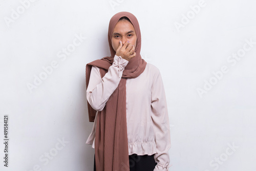 young asian beautiful muslim woman holding her nose because of a bad smelling something
