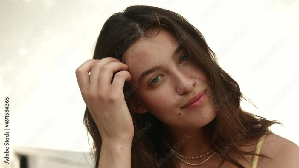 Close up portrait of beautiful young caucasian woman looking at camera on light background. Brunette straightens her hair and smiles. Fashion, beauty concept. Close up portrait of beautiful young caucasian woman looking at camera on light background. Brunette straightens her hair and smiles. Fashion, beauty concept.