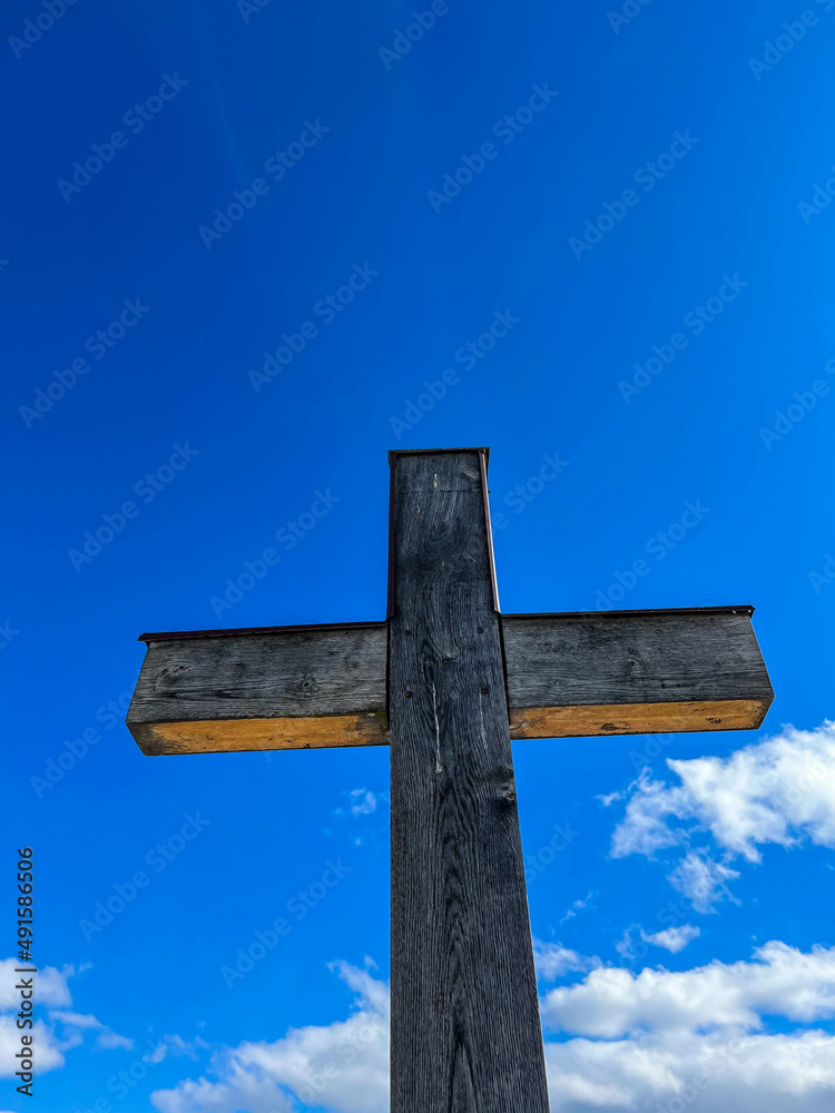 Simple oak wood catholic cross against deep blue sky with white clouds vertical image.