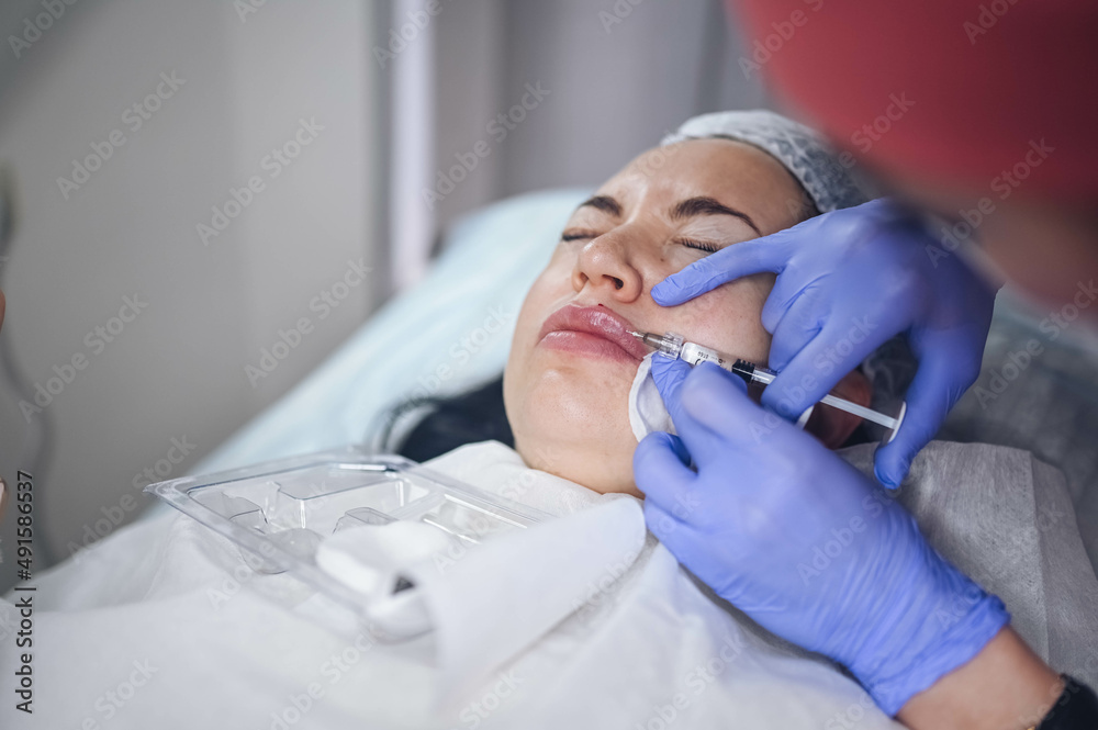 Cosmetologist doing painful lip augmentation procedure with hyaluronic
