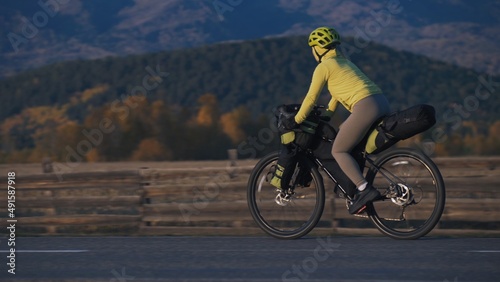 The woman travel on mixed terrain cycle touring with bikepacking. The traveler journey with bicycle bags. Sport tourism bikepacking, bike, sportswear in green black colors. Mountain snow capped. photo