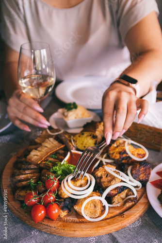 Plate with shashlyk and meat delicacies. Barbecue, baked potatoes with lard and onions. Girl's hand holds a glass of wine