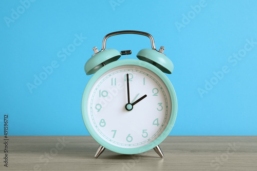 Turquoise alarm clock on wooden table against light blue background