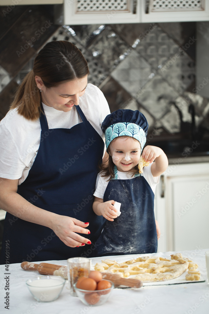 Mother and her little daughter preparing pastry in the kitchen. Little girl using metallic form to cut the dough