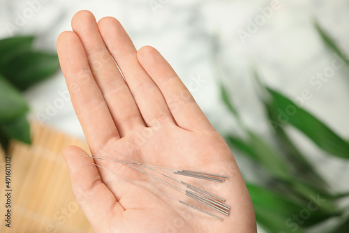 Woman holding many acupuncture needles on blurred background  top view