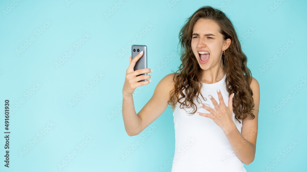 Screaming woman. Virtual connection. Angry emotion. Mad stressed lady in white dress looking smartphone holding hand isolated blue copy space. Screaming woman. Virtual connection. Angry emotion. Mad stressed lady in white dress looking smartphone holding hand isolated blue copy space.