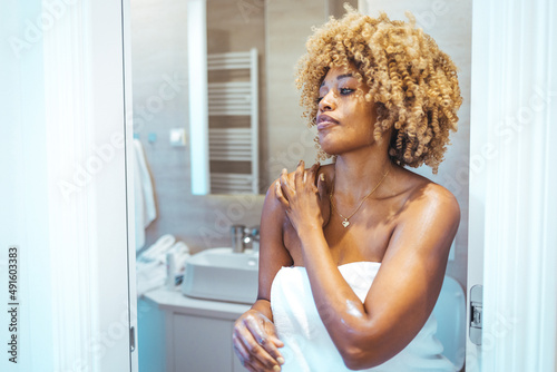 Concept of beauty procedure. Cropped view of afro american woman in bathrobe spending morning in bathroom, applying cream on soft skin. Taking care of yourself