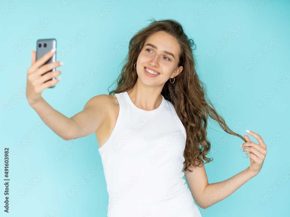 Lovely selfie. Happy woman. Virtual lifestyle. Pretty coquettish smiling lady in white dress looking smartphone posing isolated blue. Lovely selfie. Happy woman. Virtual lifestyle. Pretty coquettish smiling lady in white dress looking smartphone posing isolated blue.